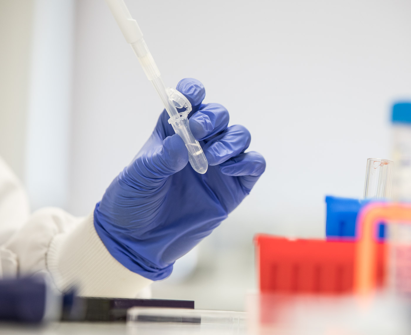 A hand wearing gloves holding a test tube in a lab setting