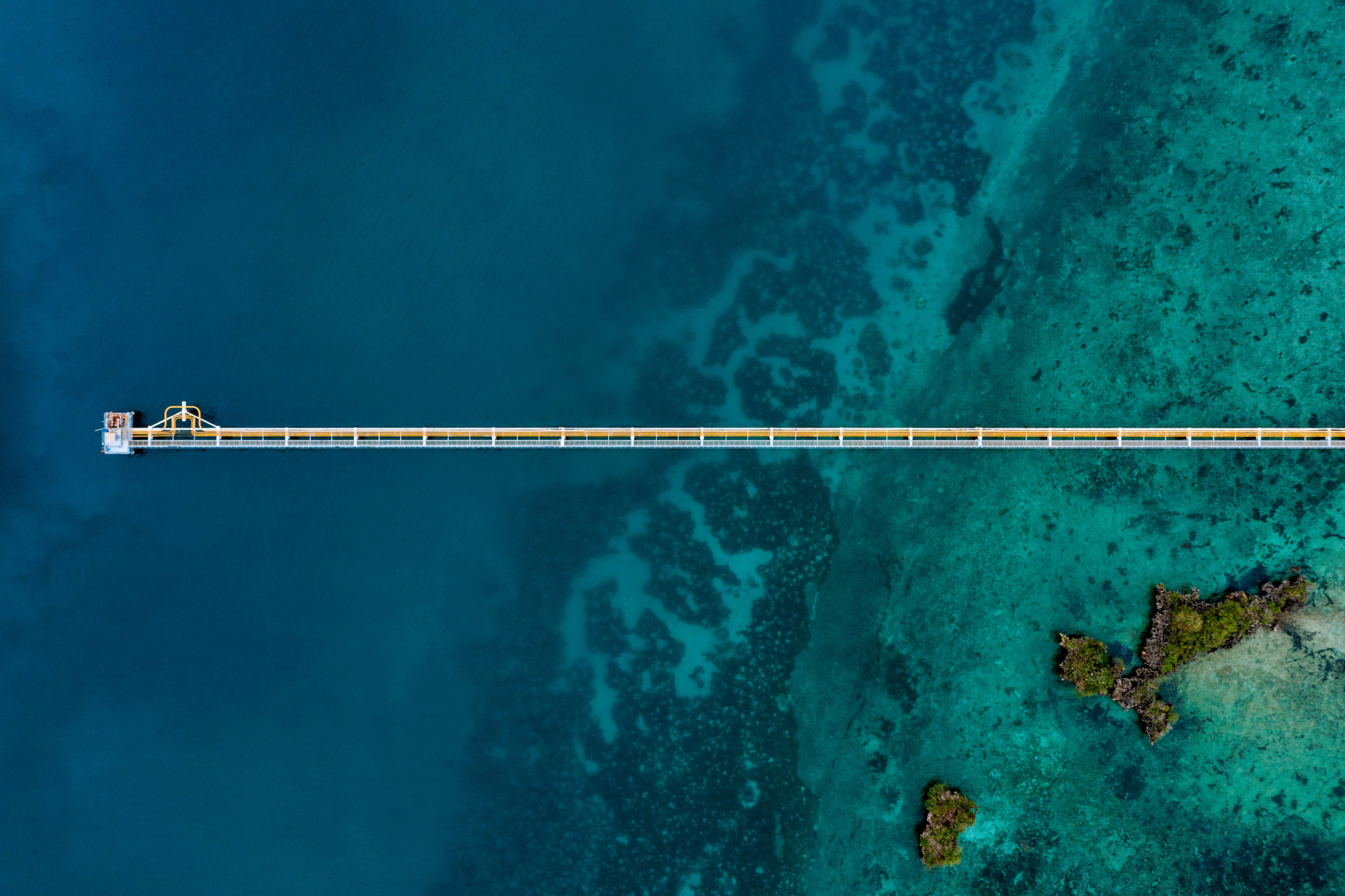 An aerial shot of an gas pipe leading out to sea over blue ocean and rocks