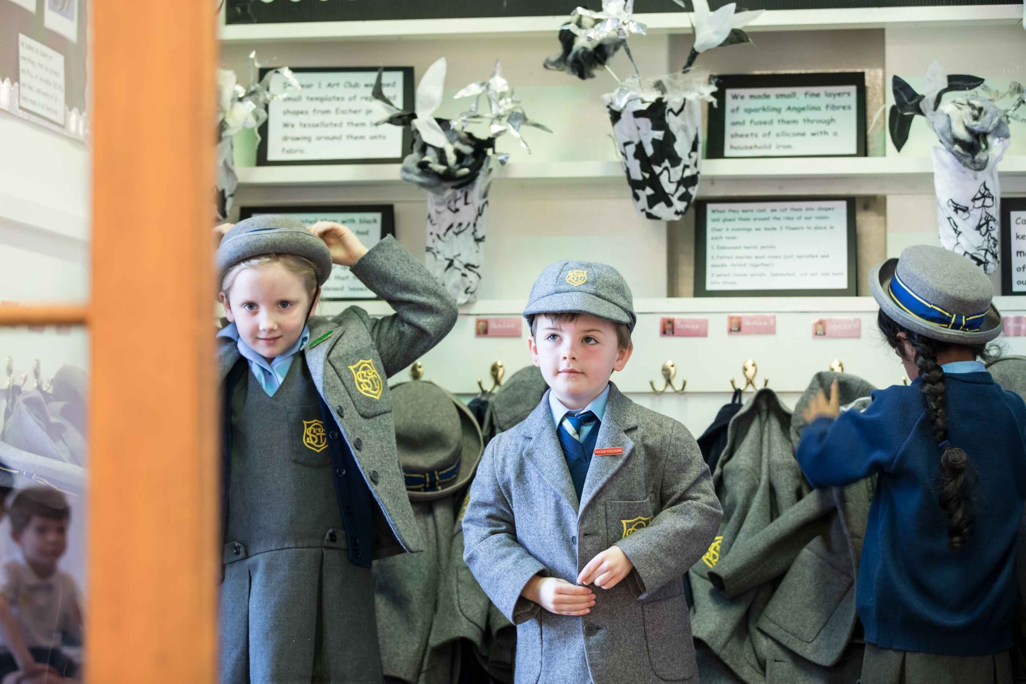 Three happy pupils put on their jackets by a coatrack in a school