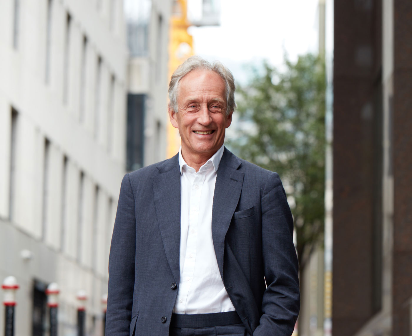 A headshot of a man standing outside looking at camera wearing a suit and open collar